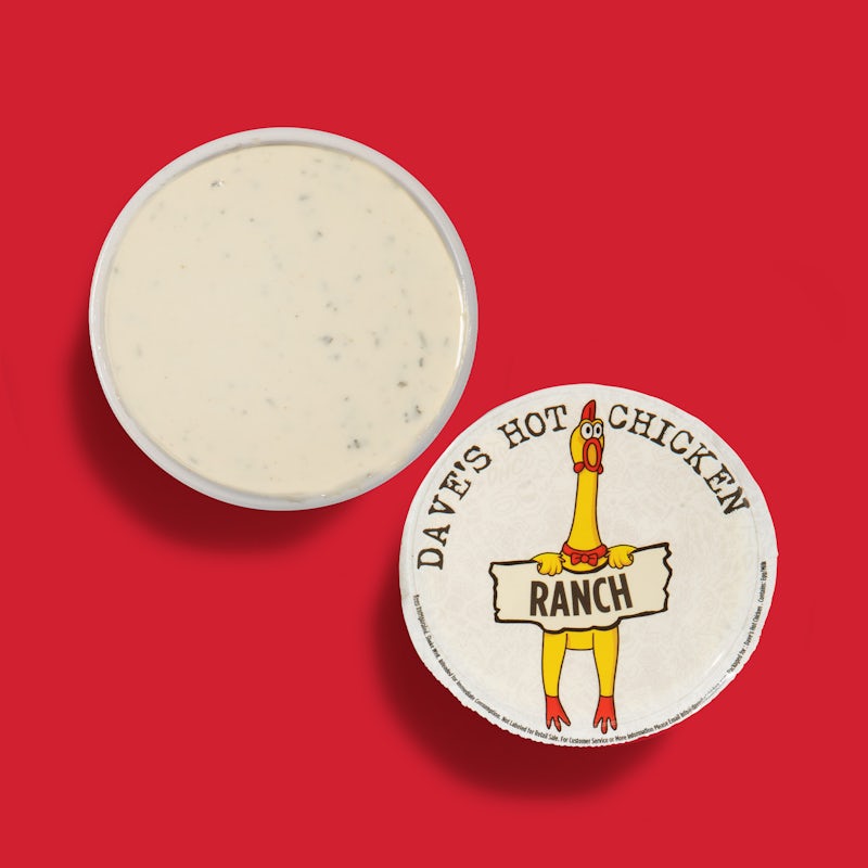 Top-down view of Dave’s Hot Chicken ranch dipping sauce cup with white branded lid on a red background.