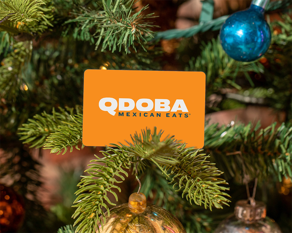 QDOBA Mexican Eats gift card hanging on a decorated Christmas tree branch with ornaments and holiday lights.