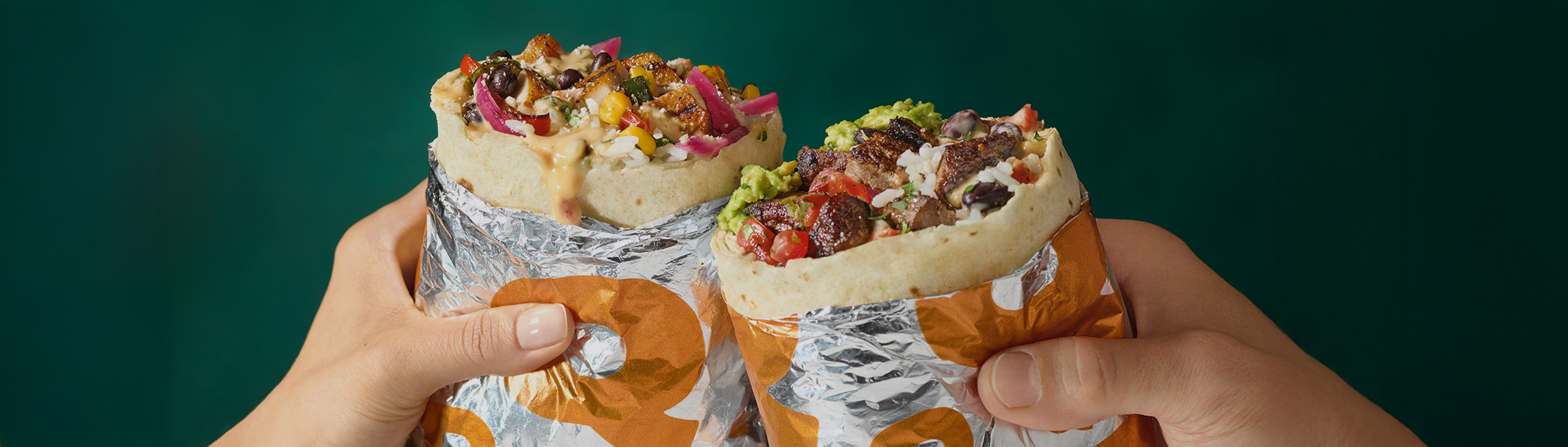Two hands holding freshly made QDOBA burritos filled with grilled steak, rice, beans, queso, guacamole, and toppings—highlighting National Burrito Day BOGO offer.