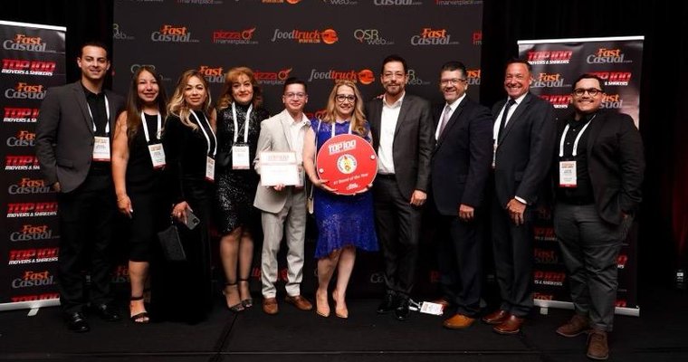 Photo of the Dave's Hot Chicken team receiving the top award at FastCasual's Top 100 Movers & Shakers gala, celebrating their remarkable success attributed to experienced multi-unit franchisees like Roaring Fork Restaurant Group. 