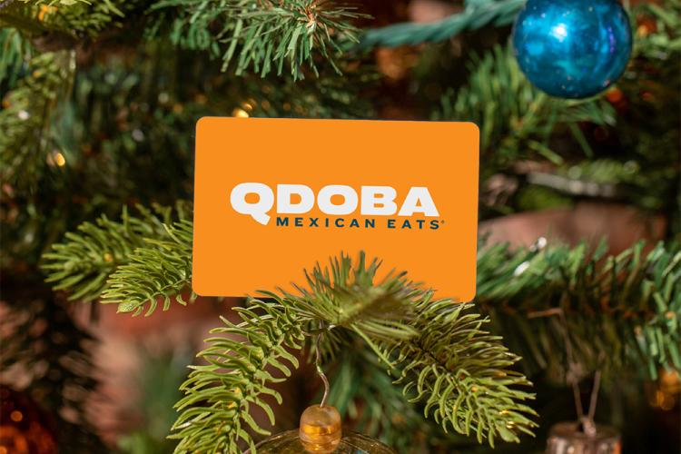 QDOBA Mexican Eats gift card hanging on a decorated Christmas tree branch with ornaments and holiday lights.