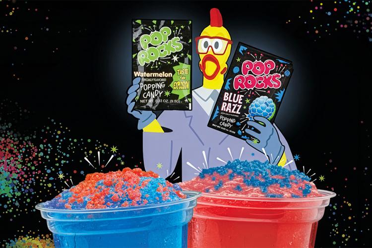 Two colorful frozen Dave’s Hot Chicken slushers topped with red and blue Pop Rocks candy sit against a black background filled with multicolored confetti-like bursts. Behind the drinks, a cartoon chicken mascot wearing 3D glasses holds packages of Watermelon and Blue Razz Pop Rocks candy. The image has a playful, high-energy neon aesthetic.